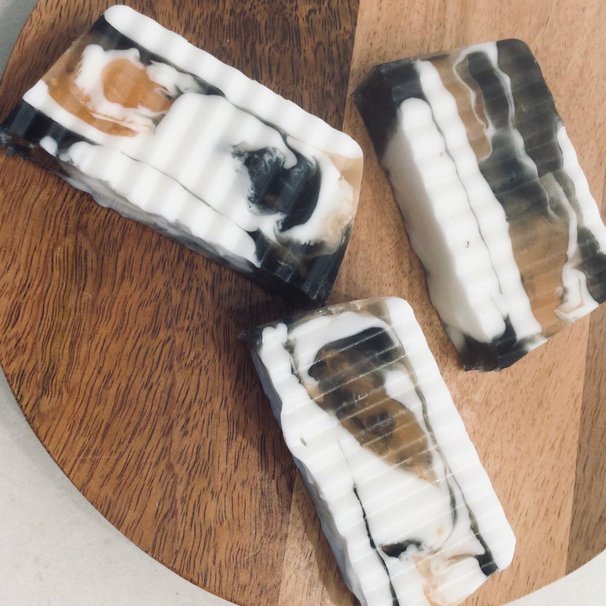 Handcrafted Soaps by SynEb Goats Milk Activated Charcoal Bar - group of three bars on round wood board
