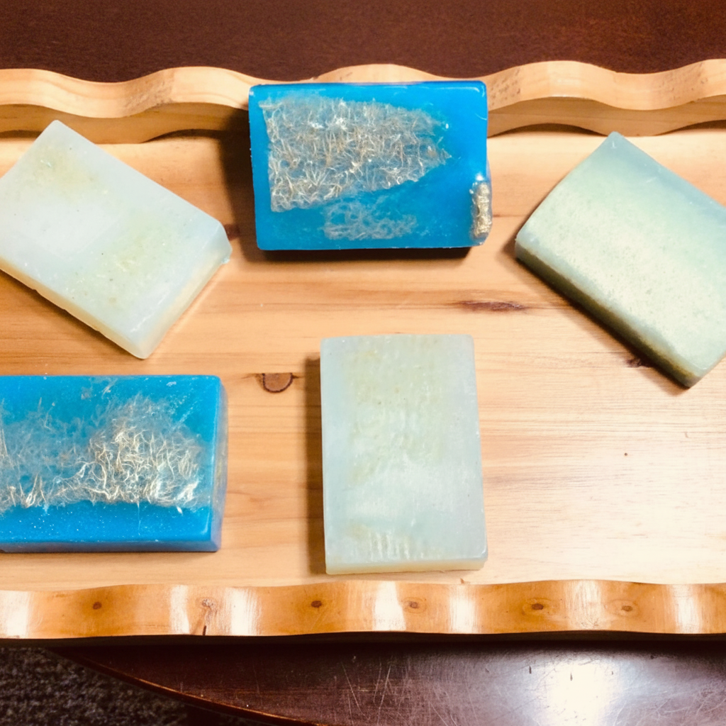Handcrafted Soaps by SynEb Organic Exfoliating Bars flat lay on wavy wood board — loofah fruit and exfoliating cloth varieties